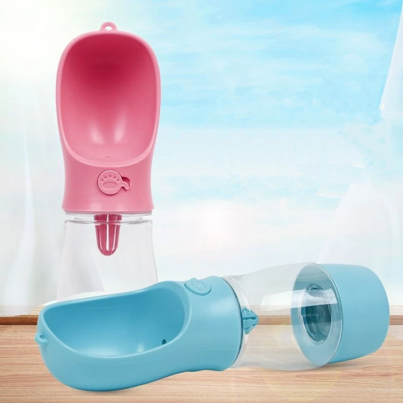 Pink and blue portable pet water bottles on a light wooden surface with a blurred outdoor background.