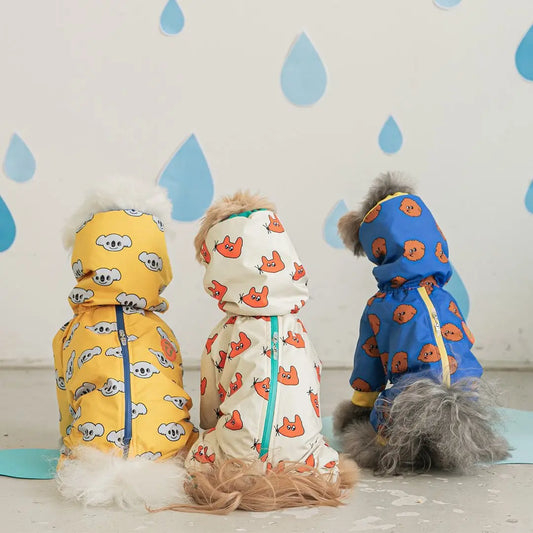 Three dogs wearing colorful raincoats with cartoon patterns against a light background with blue raindrop shapes.